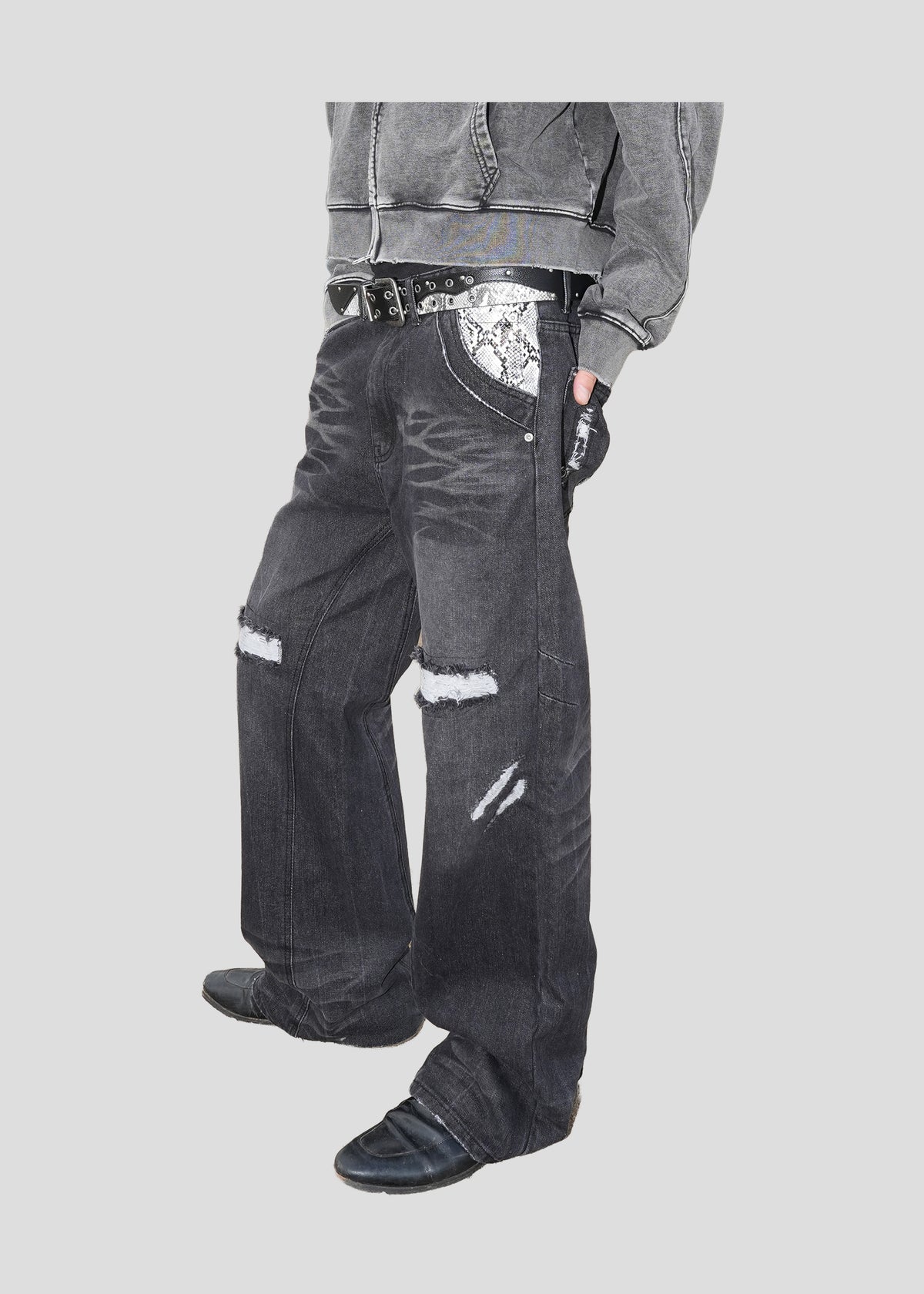 Model wearing ONEFATE Snake Jeans at an angle, showing the snake-pattern pocket panel and rips at both knees