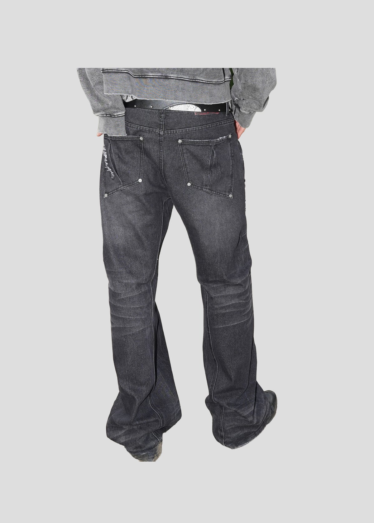Model seen from behind wearing ONEFATE Snake Jeans with a flared hem falling over black shoes