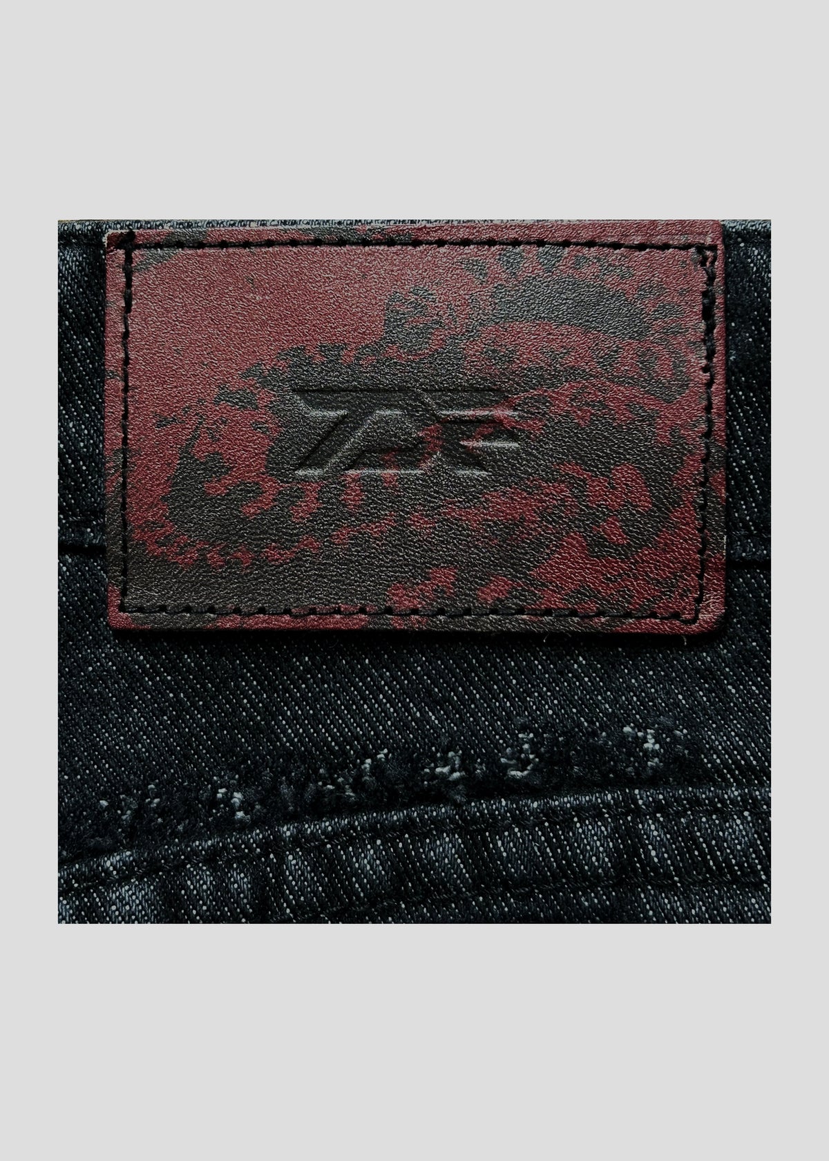 Close-up of the embossed ONEFATE logo patch on the back waistband of the Snake Jeans