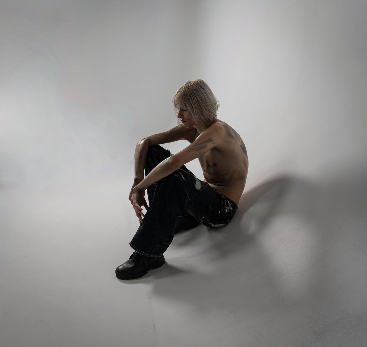 ONEFATE Campaign 01 – blond model sitting on the studio floor in black snake denim, seen from above