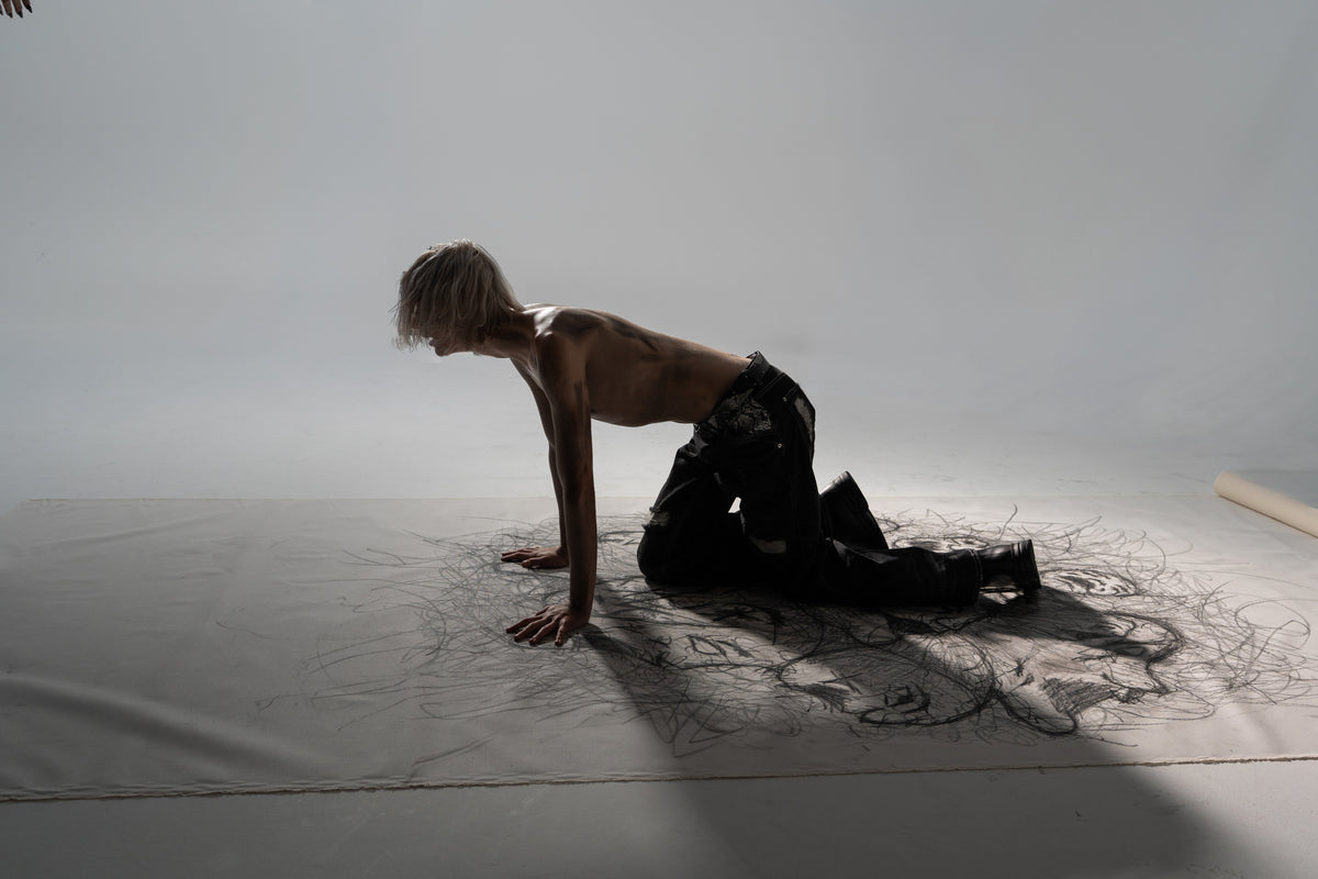 ONEFATE Campaign 01 – blond model on all fours in the studio, wearing black snake denim and snake belt
