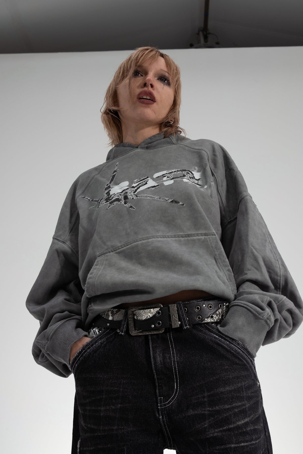 ONEFATE Campaign 01 – model in grey washed hoodie, snake belt and black snake denim, low angle
