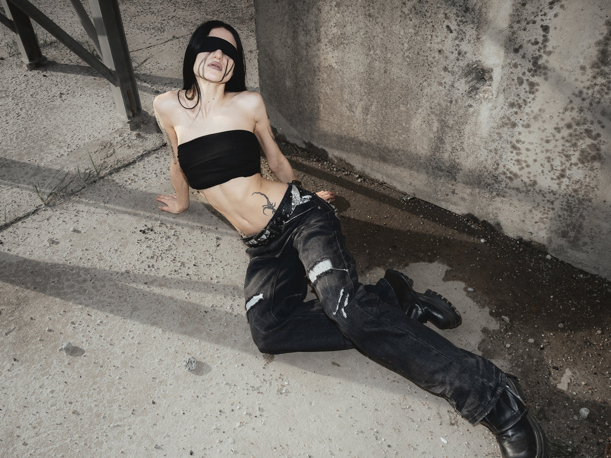 ONEFATE Campaign 02 – blindfolded model leaning back on the concrete floor in black snake denim and boots